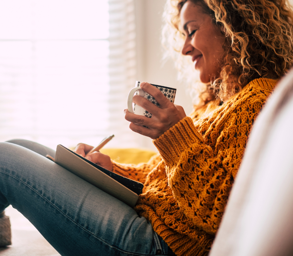 Lady relaxing on the sofa with a hot cuppa while journaling in her notebook