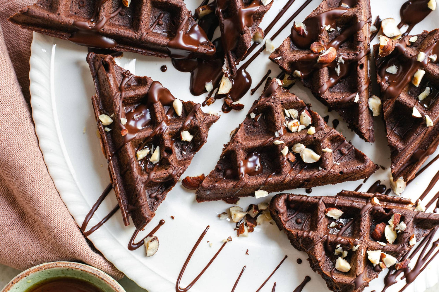 A plate of chocolate waffles drizzled in chocolate sauce and topped with chopped nuts