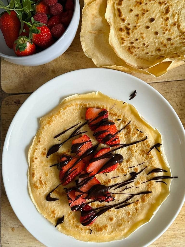 A plate loaded with crepes, topped with strawberries and drizzled with chocolate sauce.