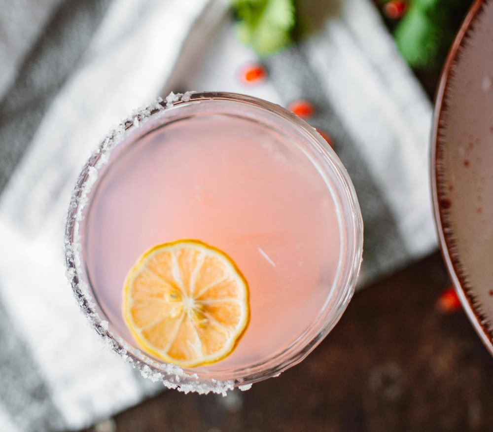 a-pink-cocktail-against-holly-berries-next-to-a-snack-bowl