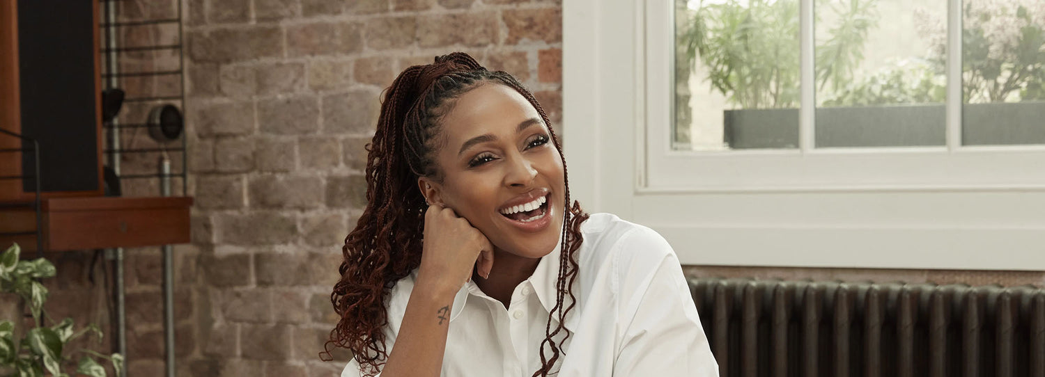 Picture of singer, Alexandra Burke, standing by a kitchen island in a kitchen, with an open bottle of Symprove whilst holding a full cup of Symprove.