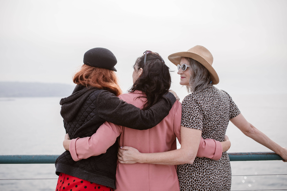 Three friends of different ages have their arms around each other on a dock