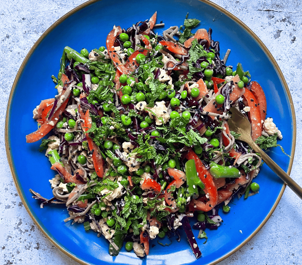 Soba noodle salad with peas, peppers and miso served up on a teal plate 