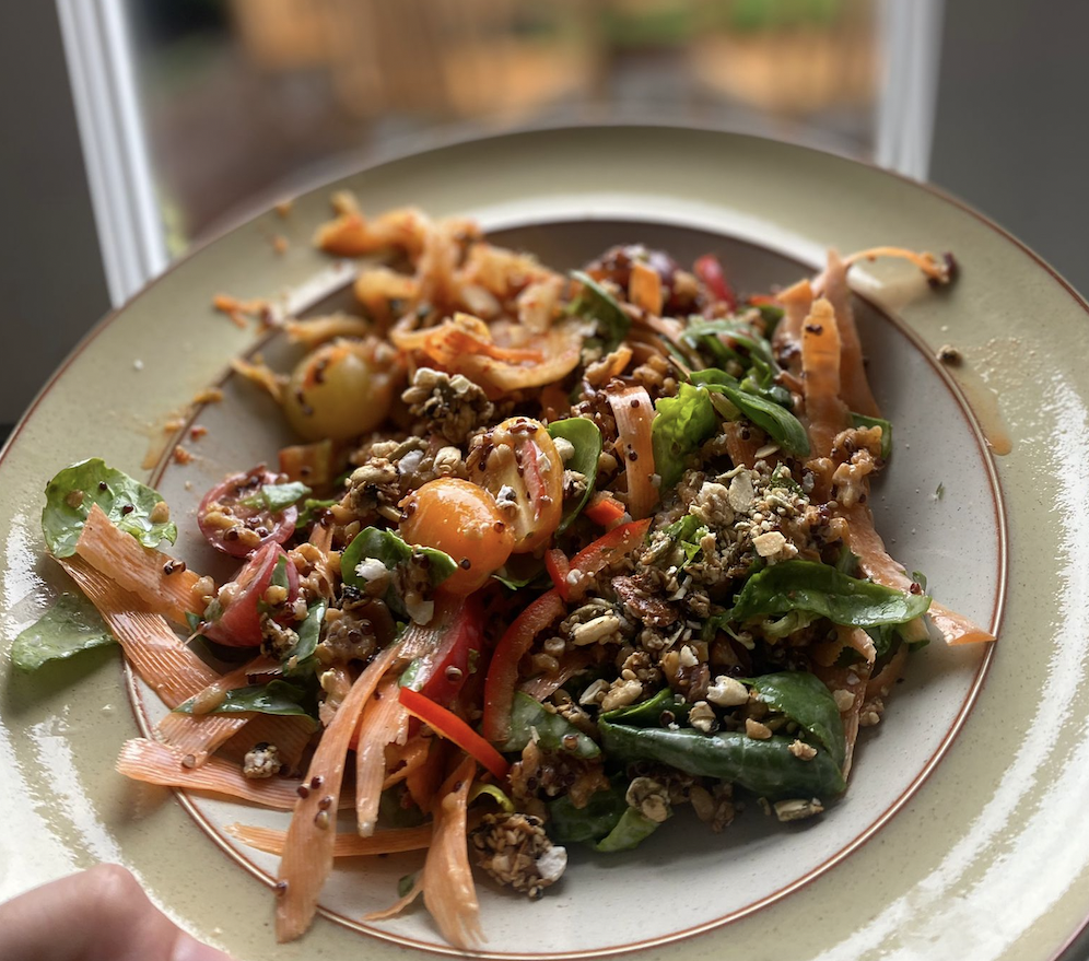 A sunshine bowl containing carrot skin, cherry tomotes, pepper, baby spinach, crunchy nuts and seeds and kefir yoghurt