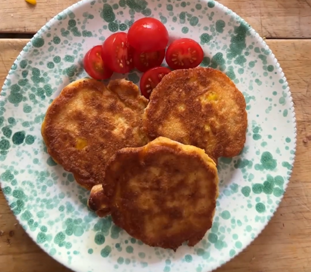 A plat of three sweetcorn fritters and a side of tomatoes