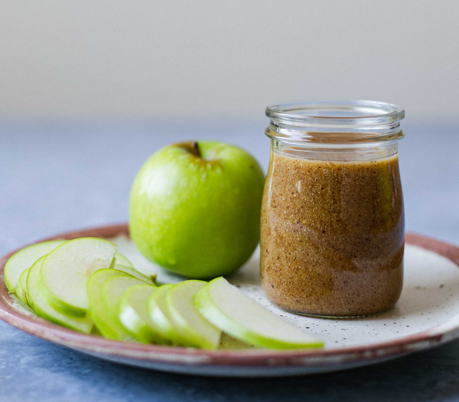 A close up picture of a plate with an apple, sliced apple pieces and jar of miso on it.