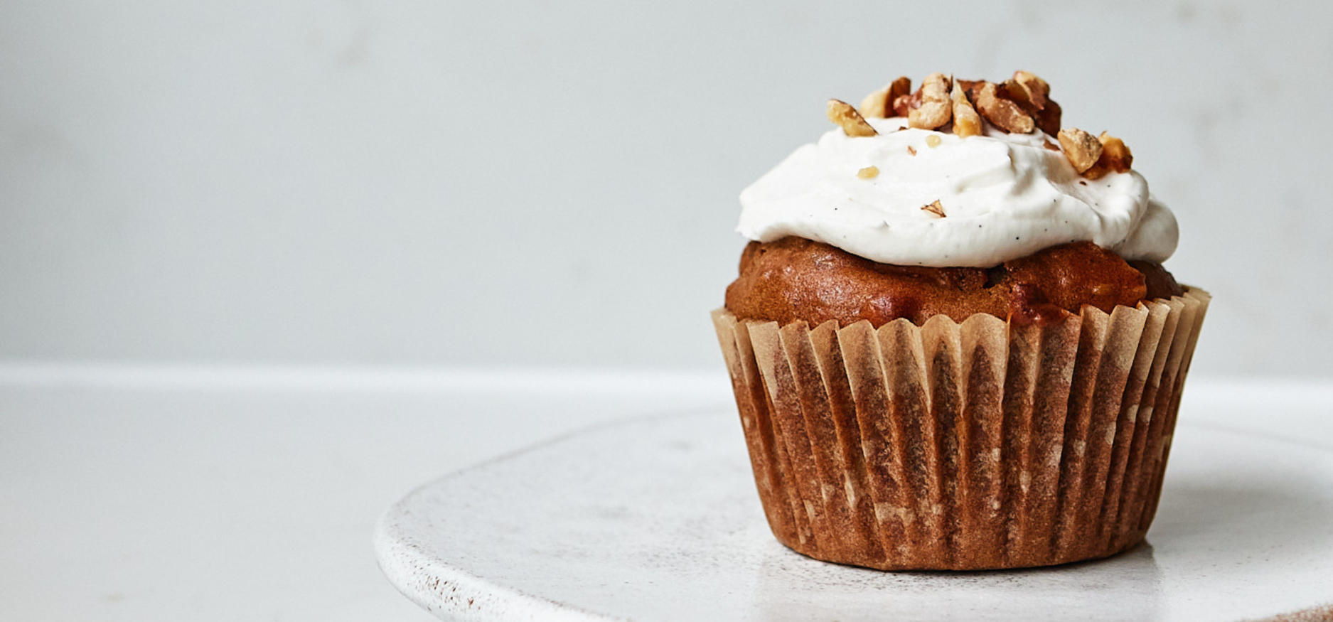 A single carrot cupcake with a coconut yoghurt and maple syrup topping with chopped nuts